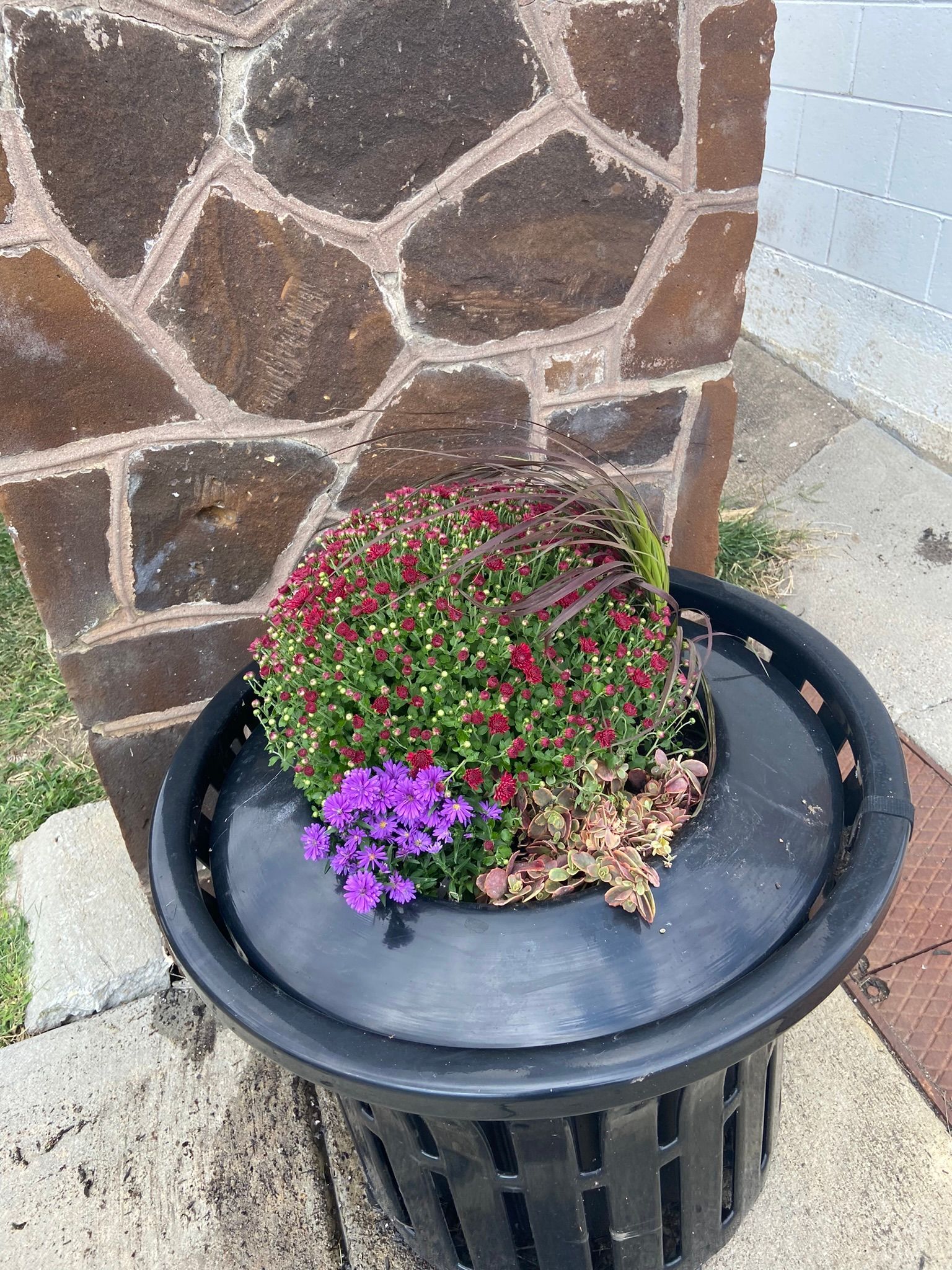 Round black planter with colorful flowers in front of a stone column.