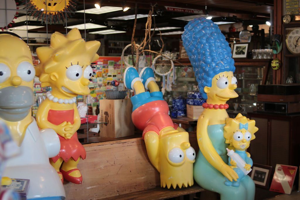 Simpsons figures: Homer, Lisa, Bart hanging, Marge with Maggie, in a store with other items.