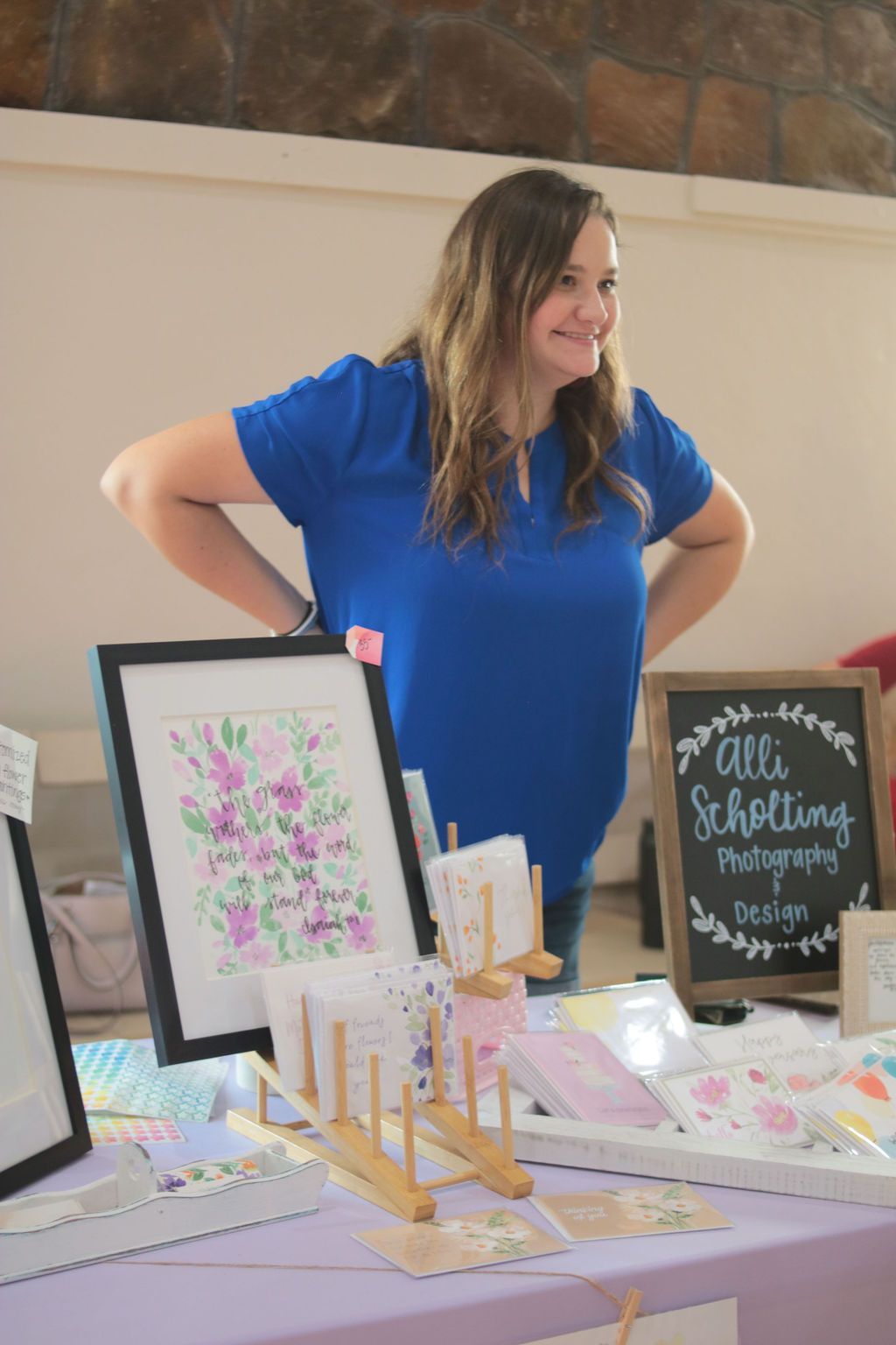 Woman at a booth, smiling, with artwork and business sign that reads 