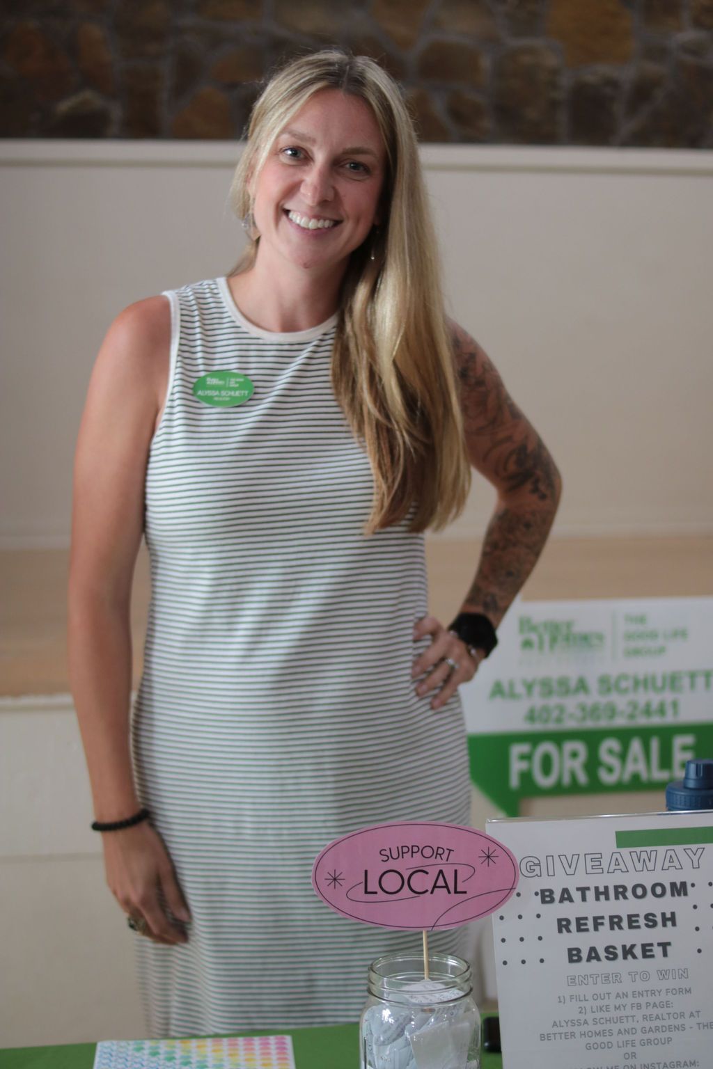 Woman with blonde hair, smiling, stands at a booth with a 