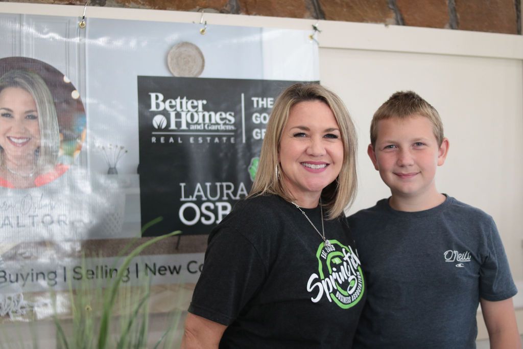 Woman and boy smiling, standing near a real estate sign.