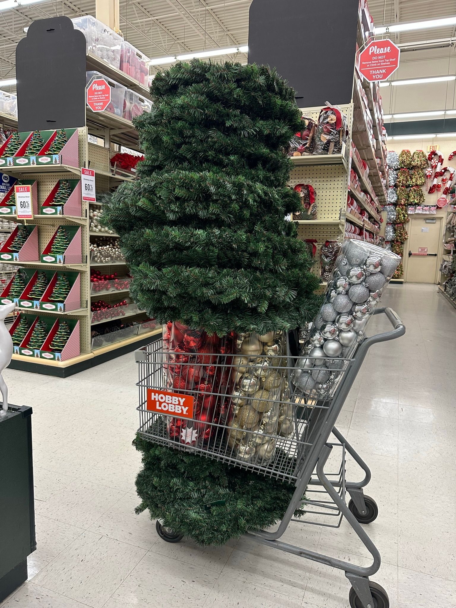 Shopping cart at Hobby Lobby filled with artificial greenery and ornaments.