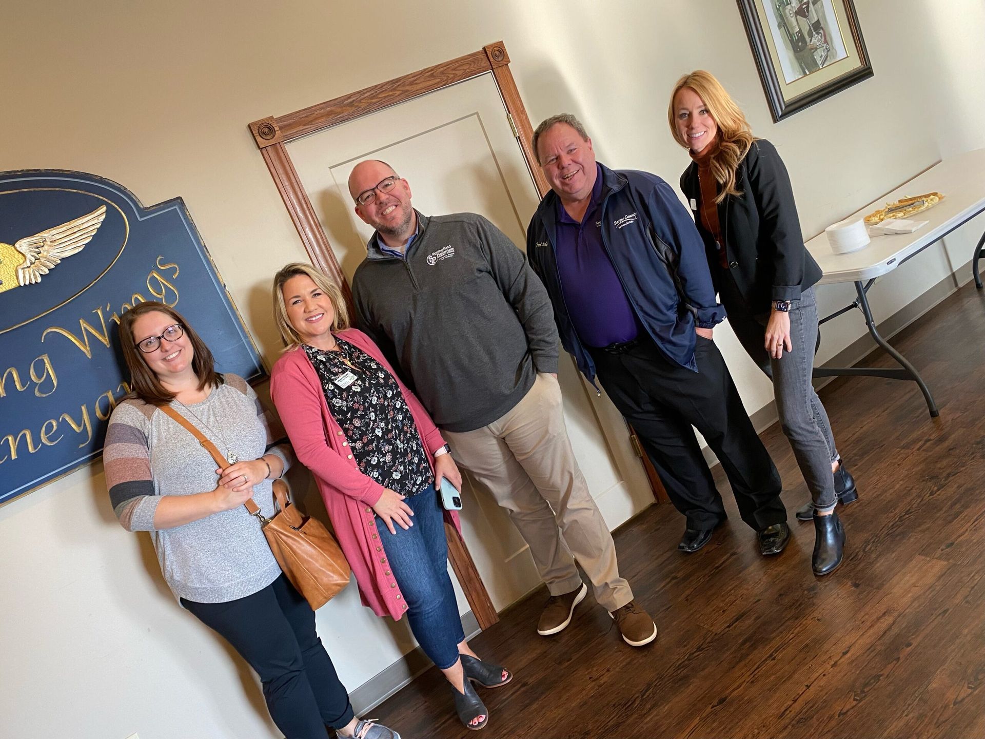 Five people pose near a sign for 