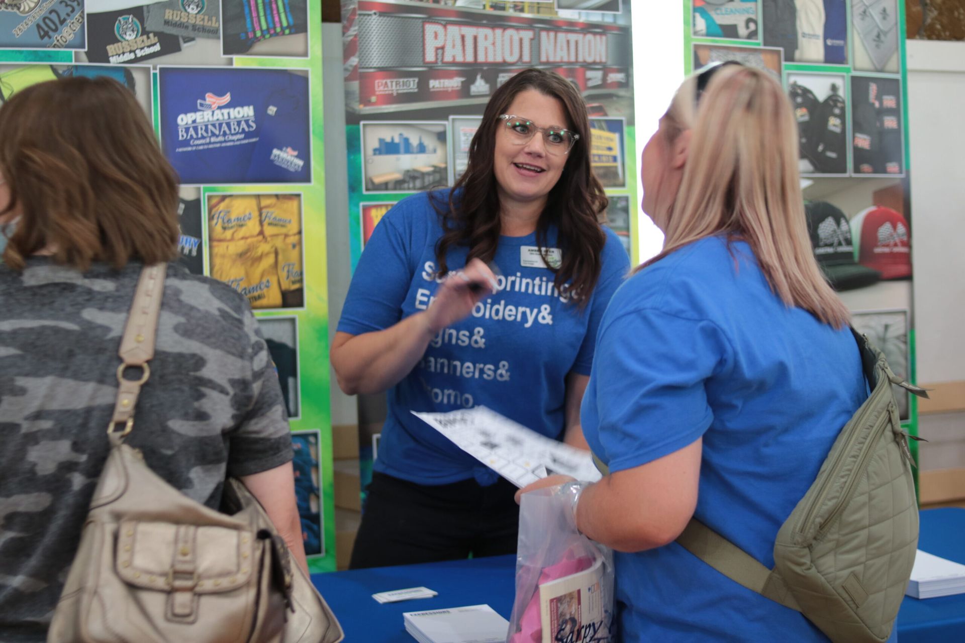 Woman at a booth talking to a customer; Patriot Nation banner in background.