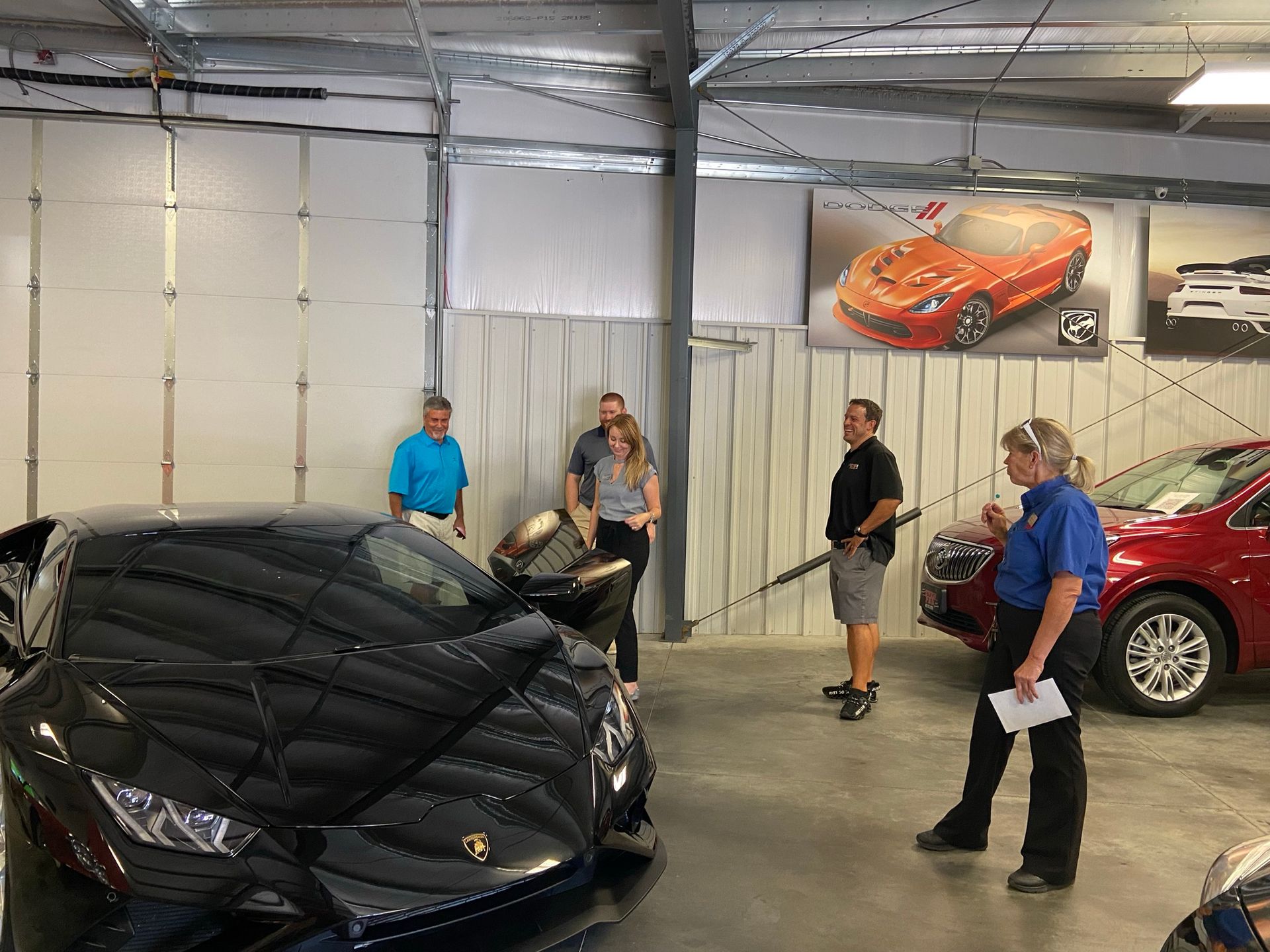 People looking at a black sports car in a showroom; a woman in a blue shirt points at the vehicle.