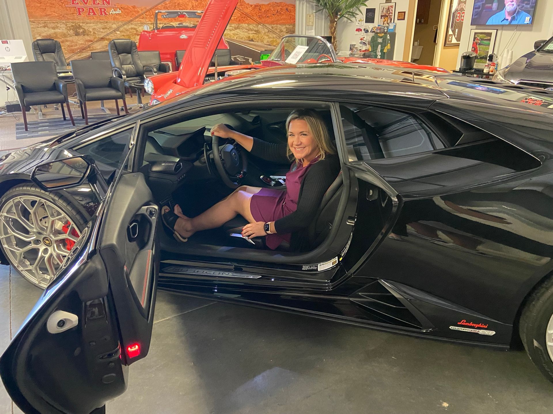 Woman sitting in black Lamborghini with door open. Inside a garage.