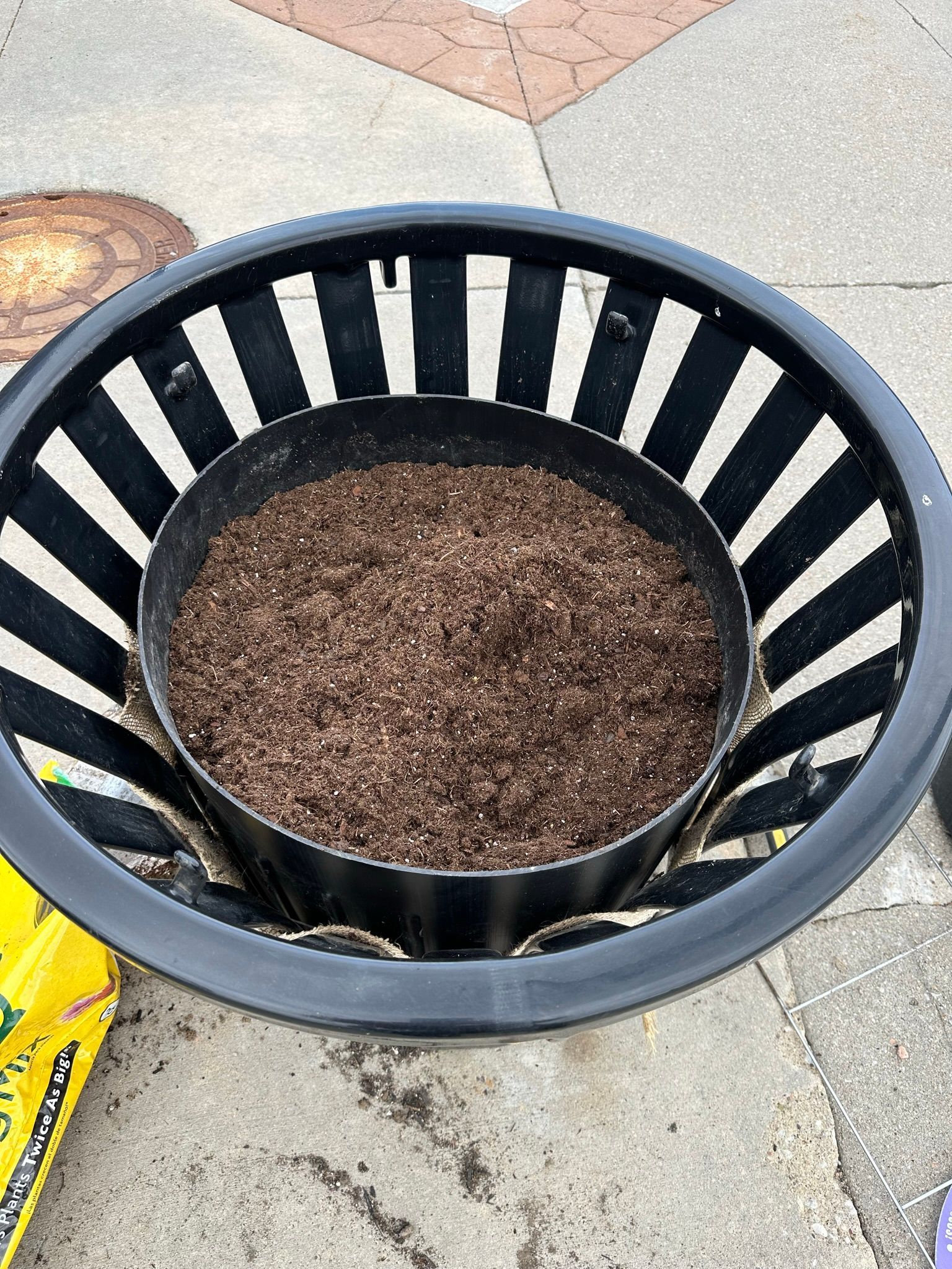 Black planter with soil inside, nested within a larger black and white striped planter.