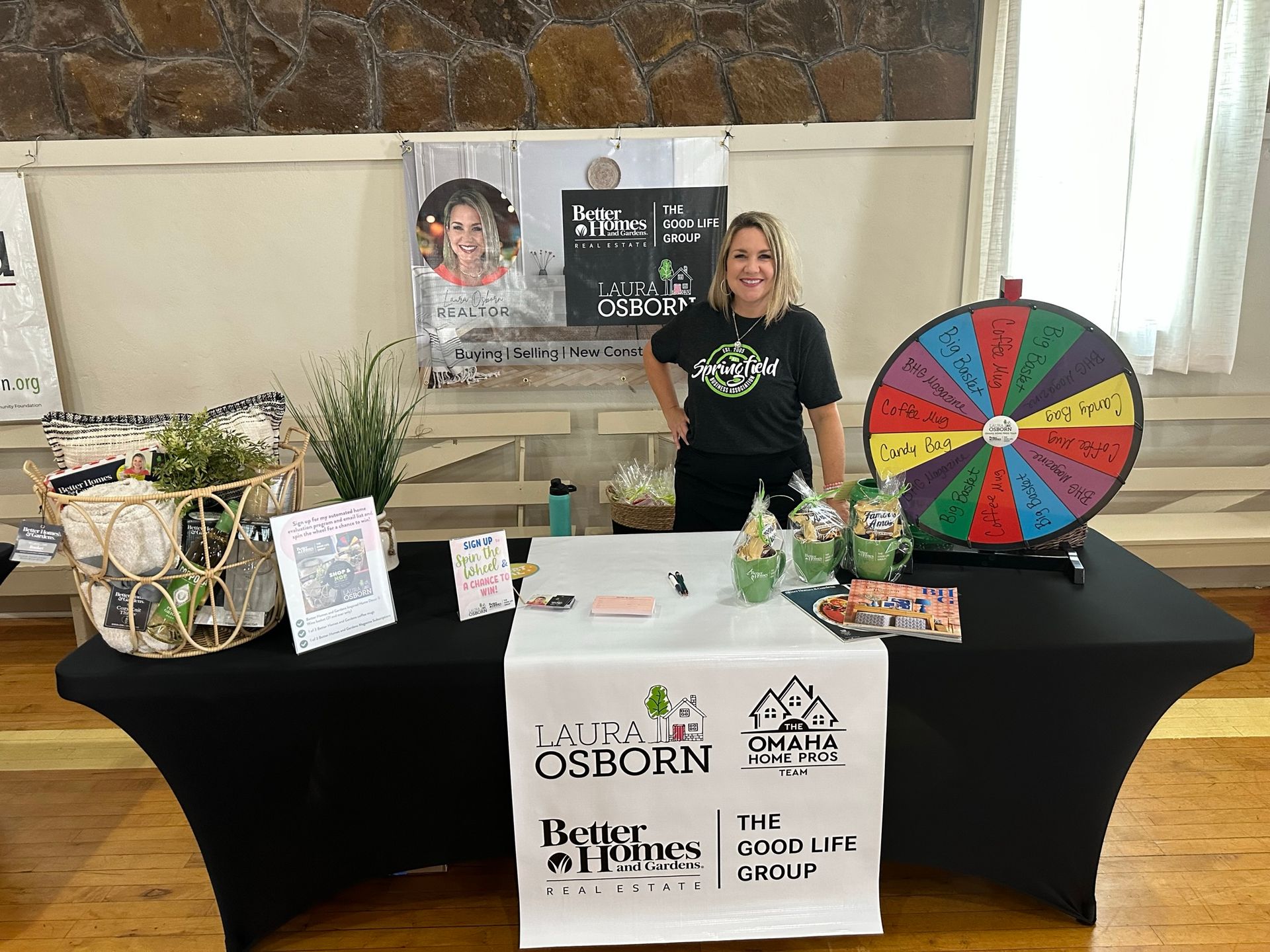 Woman stands at a Better Homes and Gardens booth with a prize wheel.