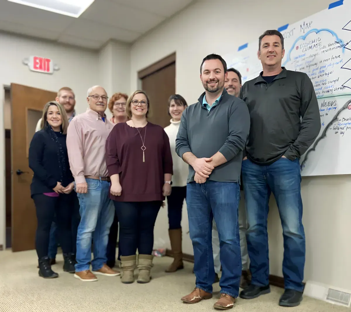 Group of colleagues standing in an office next to a whiteboard with writing.