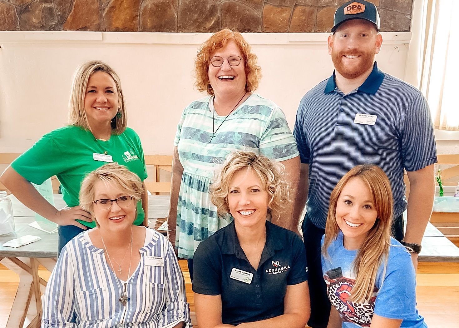 Group of six people smiling in a room. Some are standing, and some are seated.
