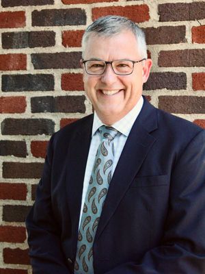 A man in a suit and tie is smiling in front of a brick wall.