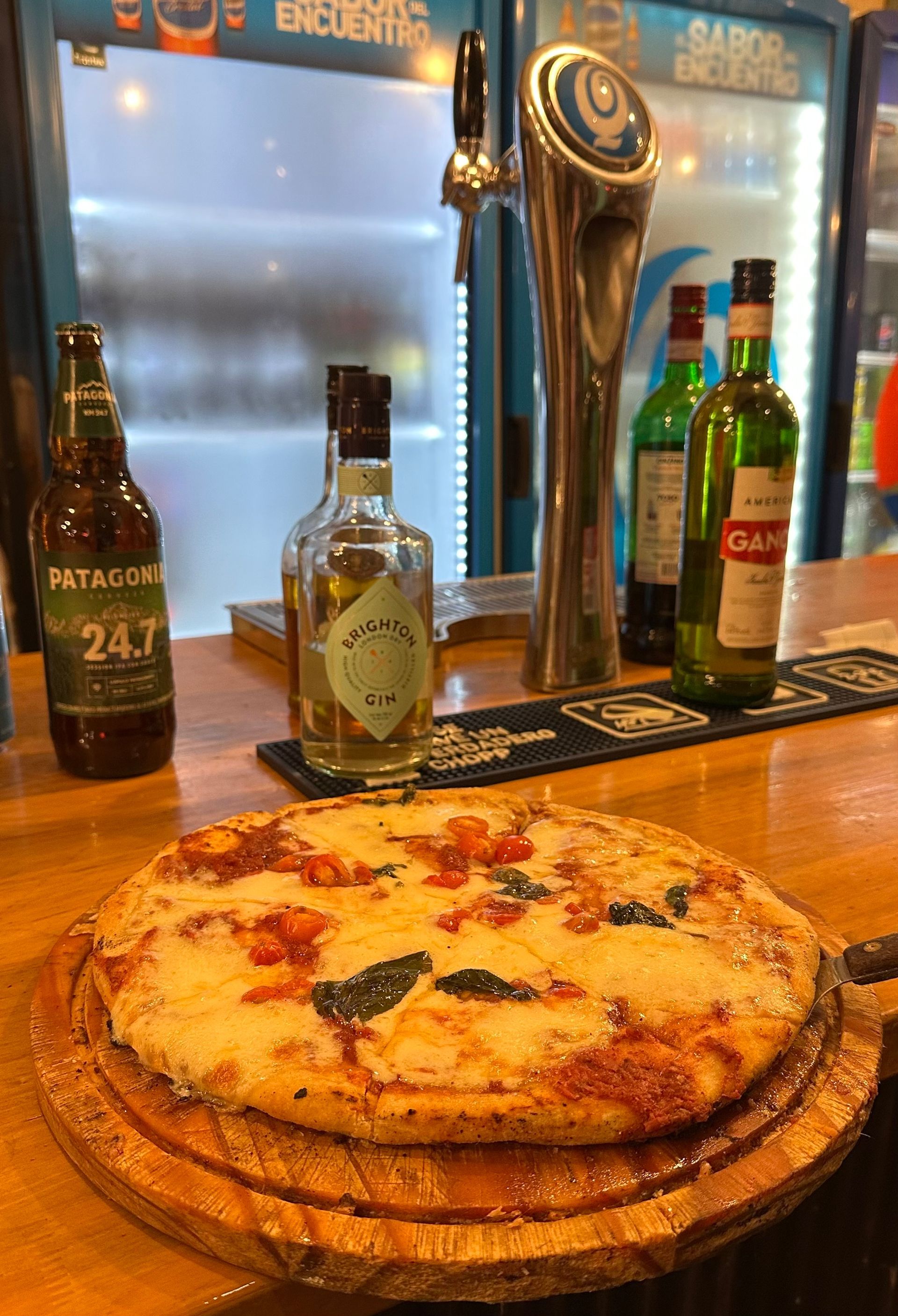 Una pizza está colocada encima de una tabla de cortar de madera sobre una barra.