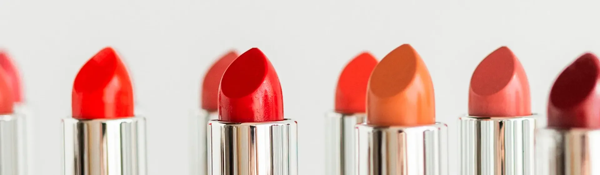 Fila de lápices labiales con varios tonos de rojo, naranja y rosa sobre un fondo blanco.
