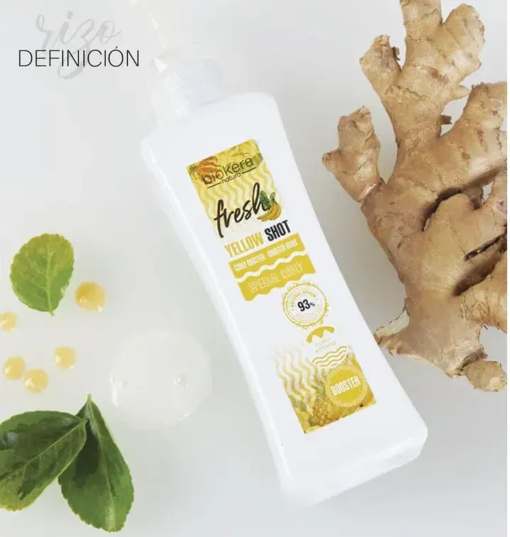 Una botella de chupito amarillo fresco junto a un trozo de jengibre.