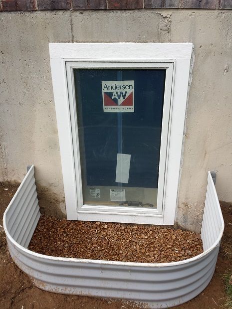 A house under construction with a window well in the ground.