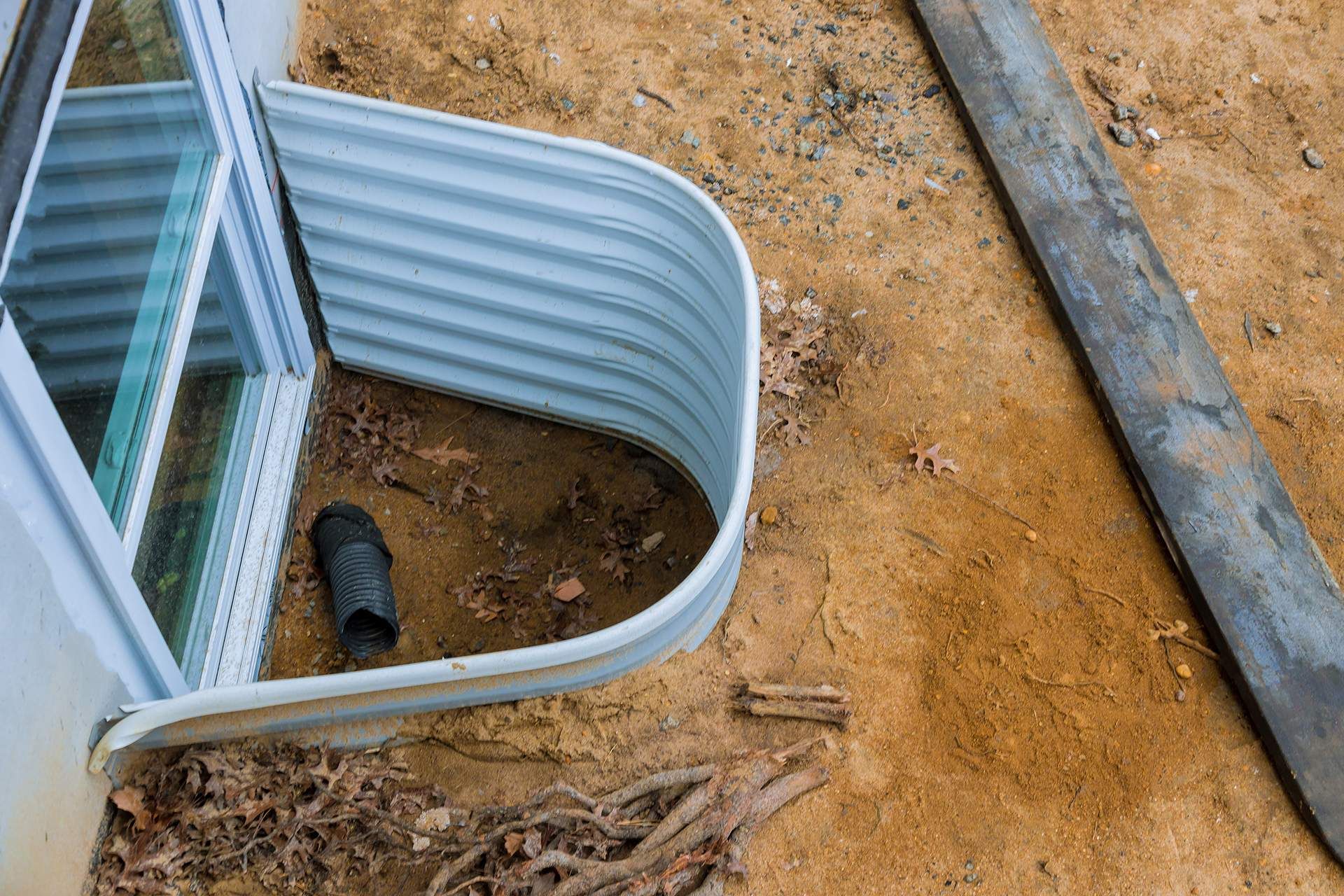 A window well is being built in the dirt next to a house.