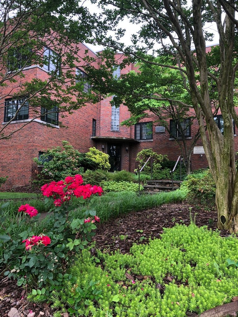 A brick building with a lush green garden in front of it.