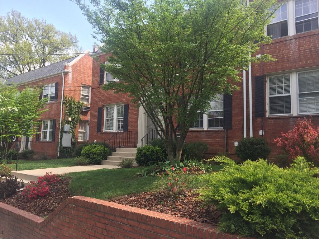 A brick apartment building with a lush green lawn and trees in front of it.
