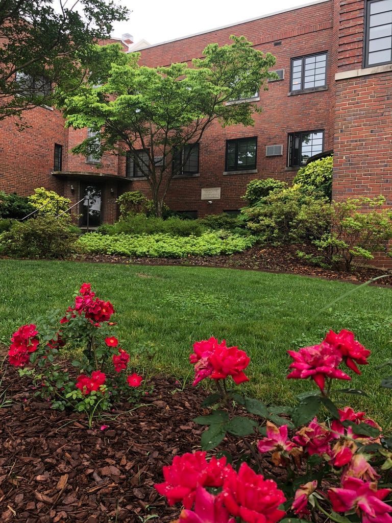 A brick building with a lush green lawn and red flowers in front of it.