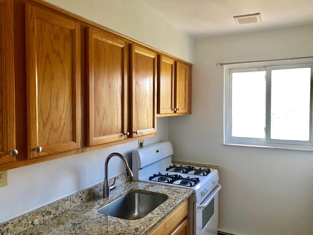A kitchen with wooden cabinets , a stove , a sink and a window.
