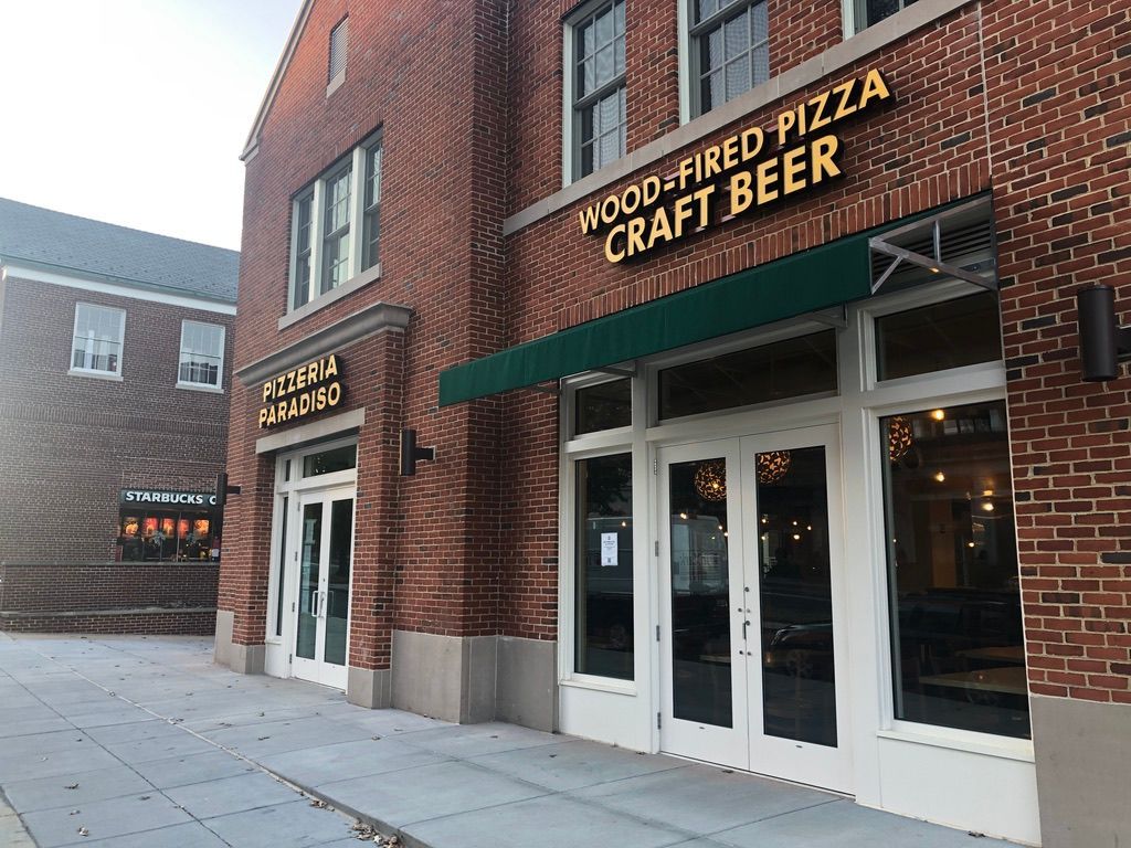 A brick building with a green awning that says wood fired pizza craft beer