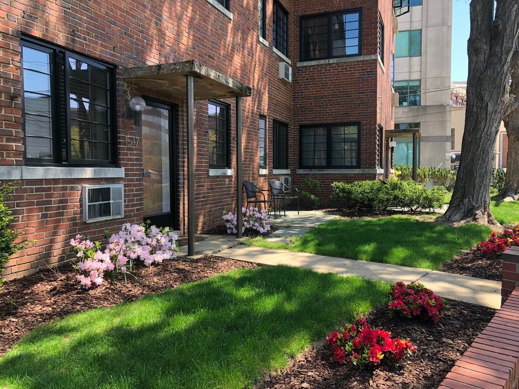 A brick apartment building with a lush green lawn and flowers in front of it.