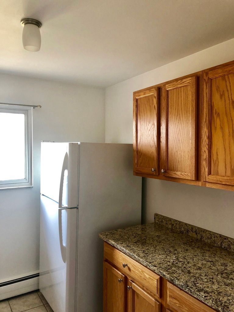 A kitchen with wooden cabinets , granite counter tops , a refrigerator and a window.