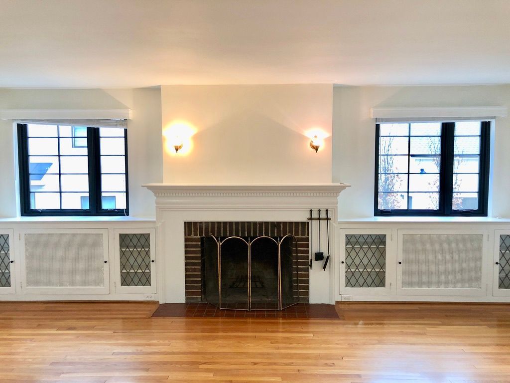 An empty living room with a fireplace and two windows.