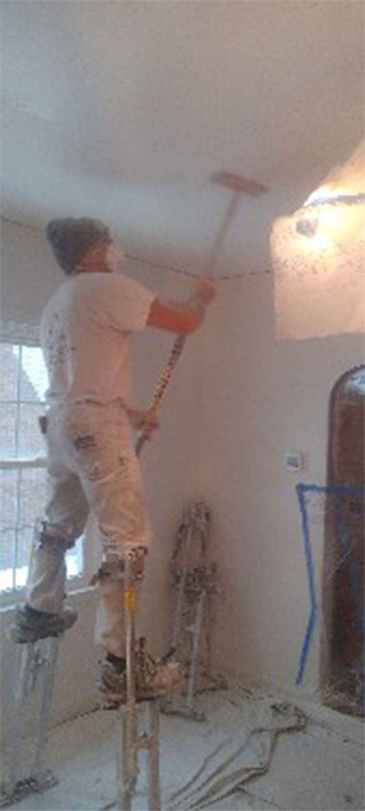 A man is standing on a ladder painting the ceiling of a room.