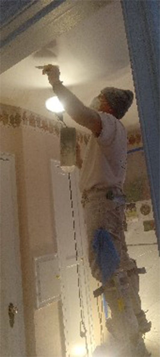 A man is painting the ceiling of a room with a brush.