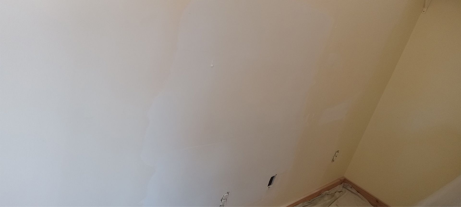 A corner of a room with a white wall and a wooden floor.