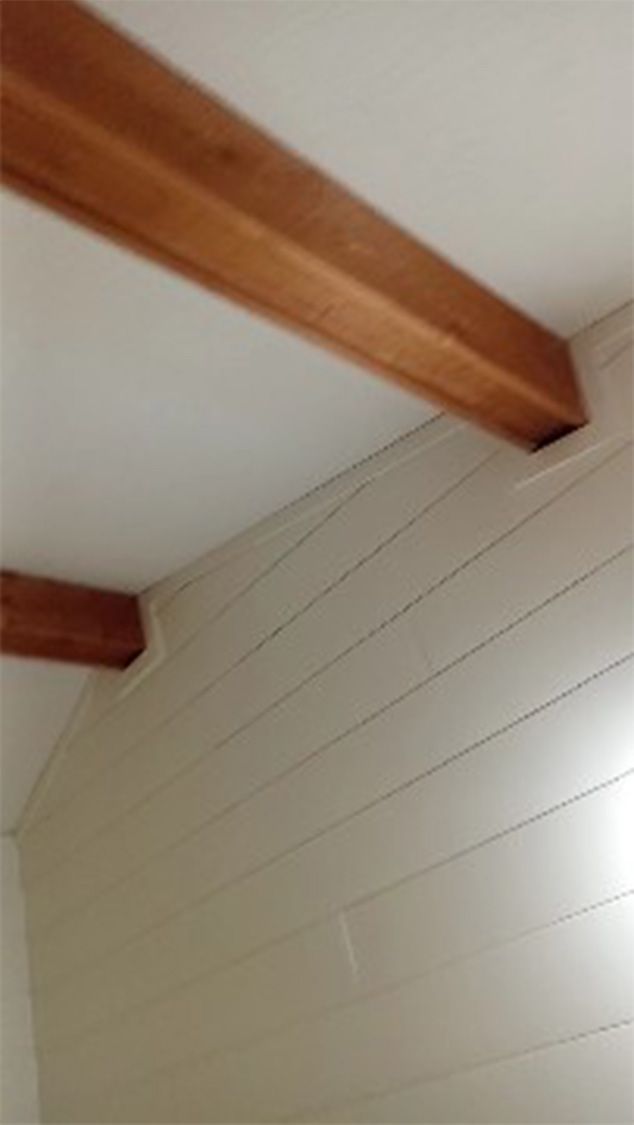 A close up of a ceiling with wooden beams and a white wall.