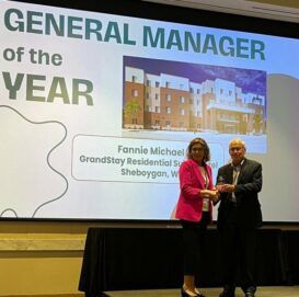 Two people standing in front of a large screen that says general manager of the year