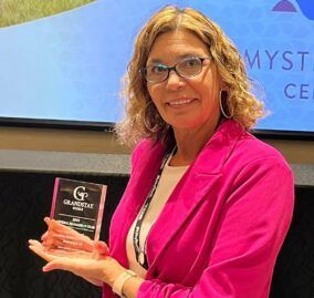 A woman in a pink jacket and glasses is holding a trophy.