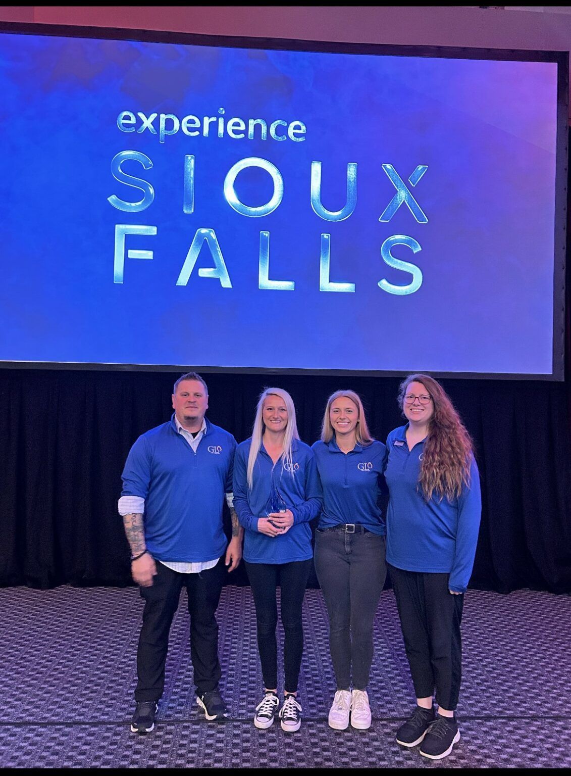 A group of people standing in front of a screen that says experience sioux falls.