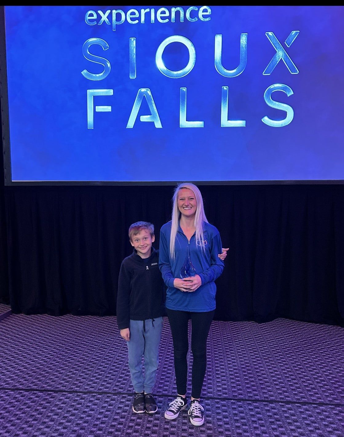 A woman and a boy are standing on a stage in front of a sioux falls sign.