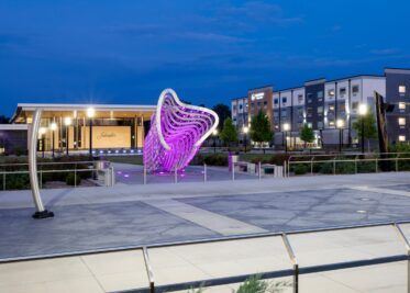 A purple sculpture is lit up in front of a building at night.