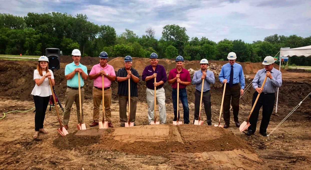 A group of construction workers are standing in the dirt with shovels.