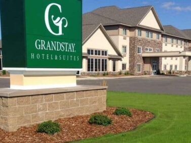 A green grandstay hotel and suites sign in front of a large building