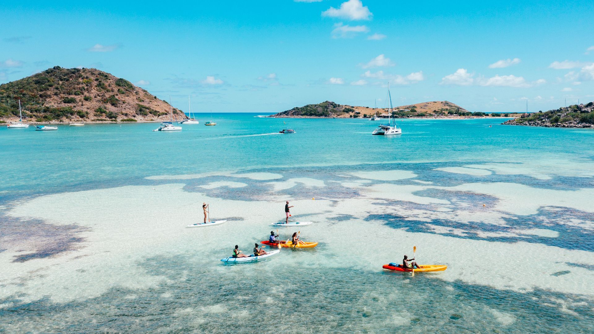 Drone view of Cul-de-Sac Bay in Saint Martin, showing a group of colorful kayaks and paddleboards gliding over the shallow sandbar in turquoise water.
