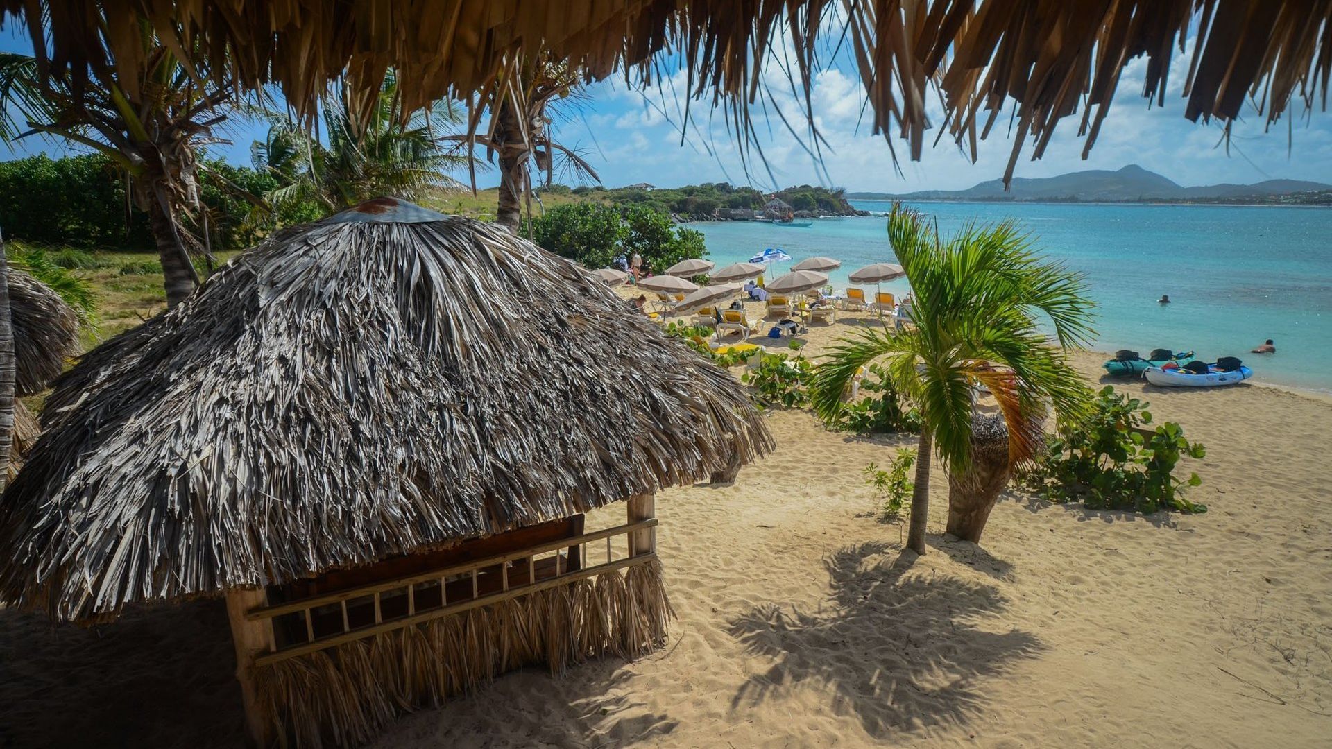 There is a hut on the beach with a thatched roof.