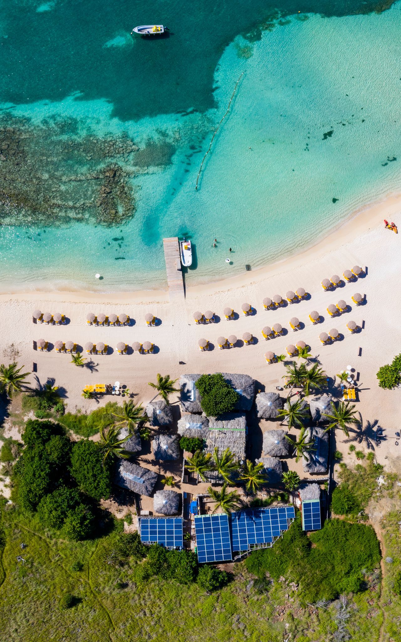Aerial view of The Yellow Beach restaurant on Pinel Island, showing the beachfront, sun loungers, and colorful umbrellas under the tropical sun.