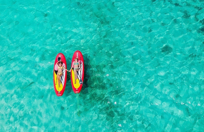 Two girls laying on their red paddle boards above turquoise waters