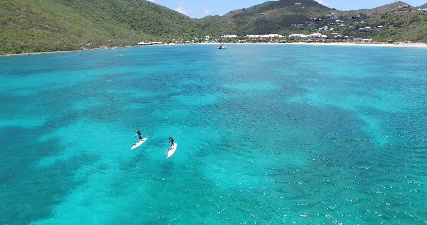 A couple of people are riding paddle boards in the ocean.
