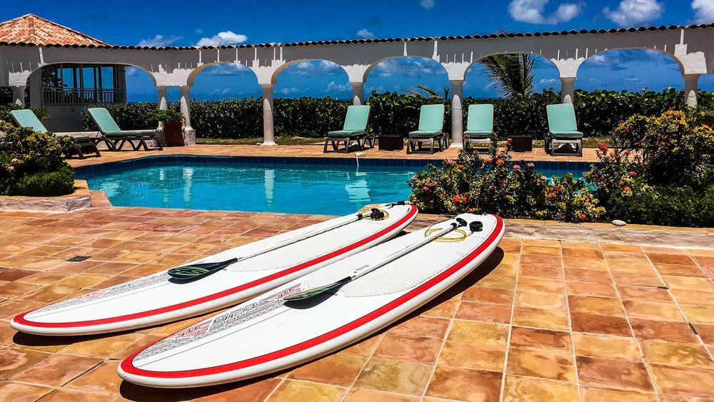 Two surfboards are sitting on a tiled patio next to a swimming pool.