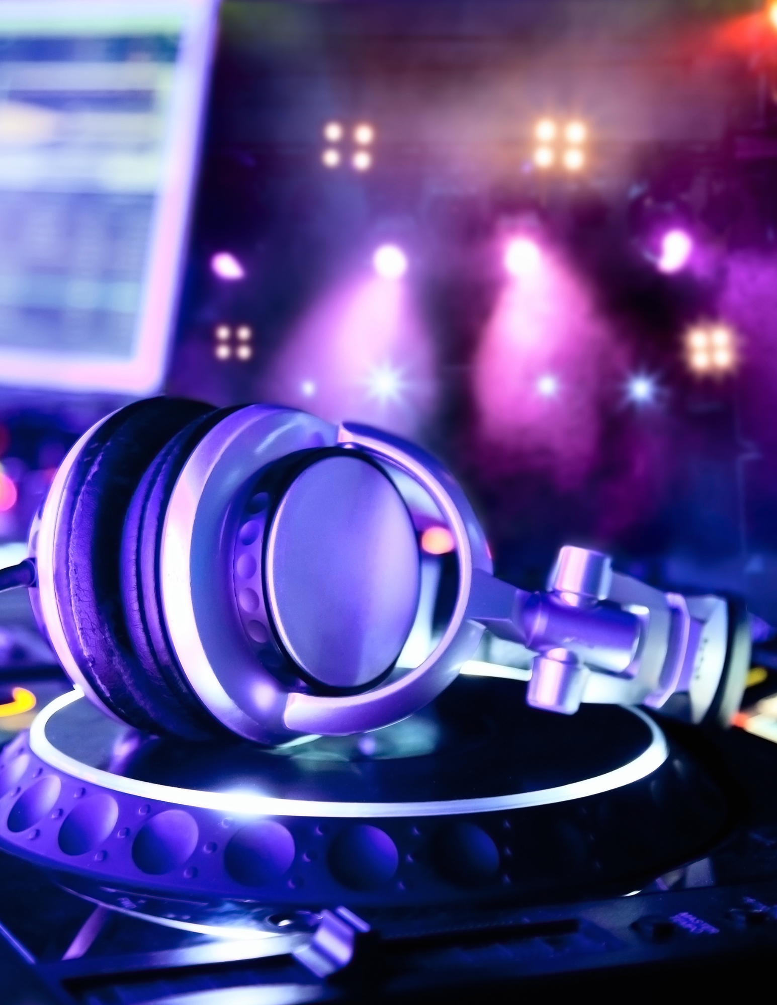Headphones rest on a turntable, stage lit with purple and bright lights.