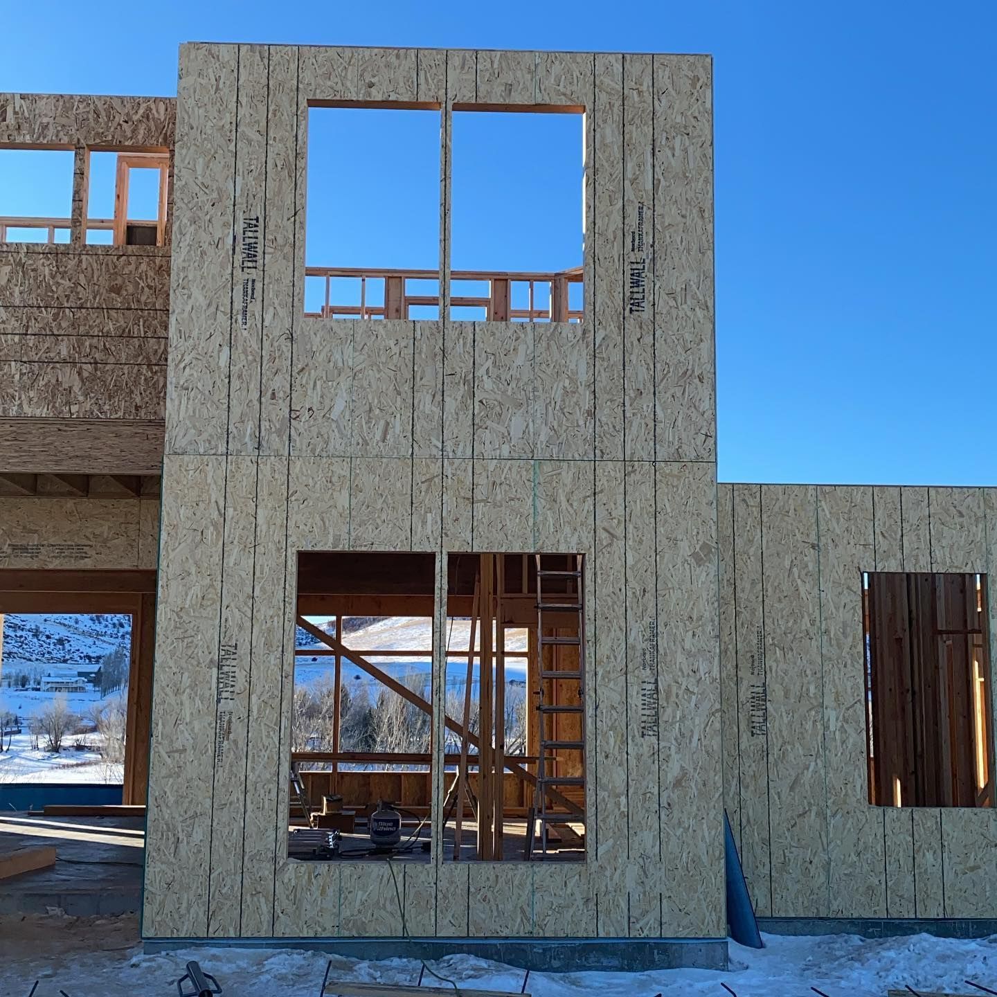 Exterior of a house under construction. OSB walls with window frames against a clear blue sky.