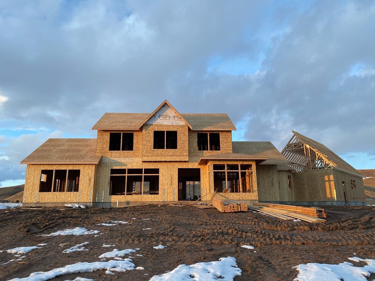 House under construction, wood frame, windows, cloudy sky, snow on ground.