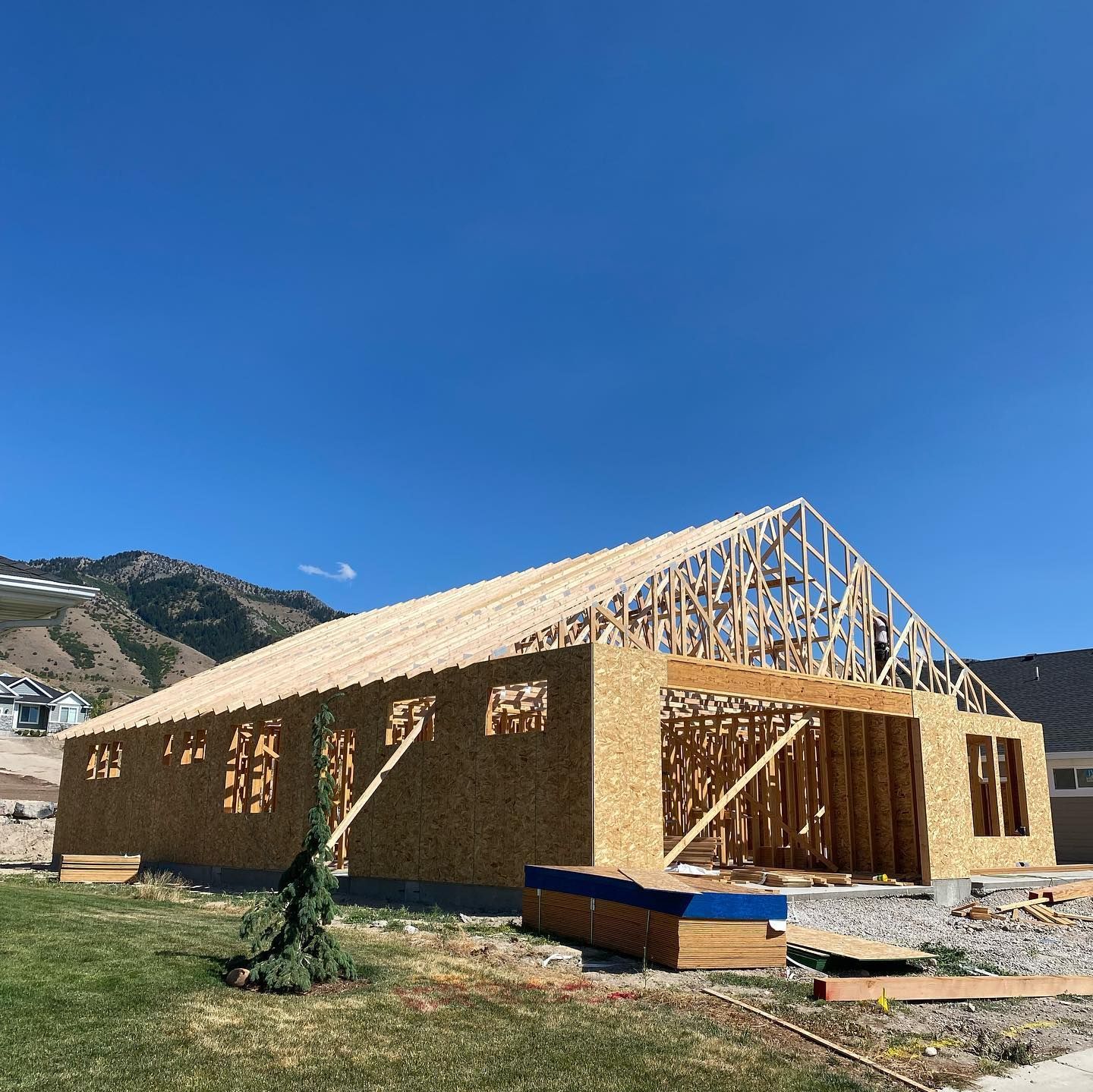 Construction of a single-story building with a wood frame roof. Mountains in the background. Sunny day.