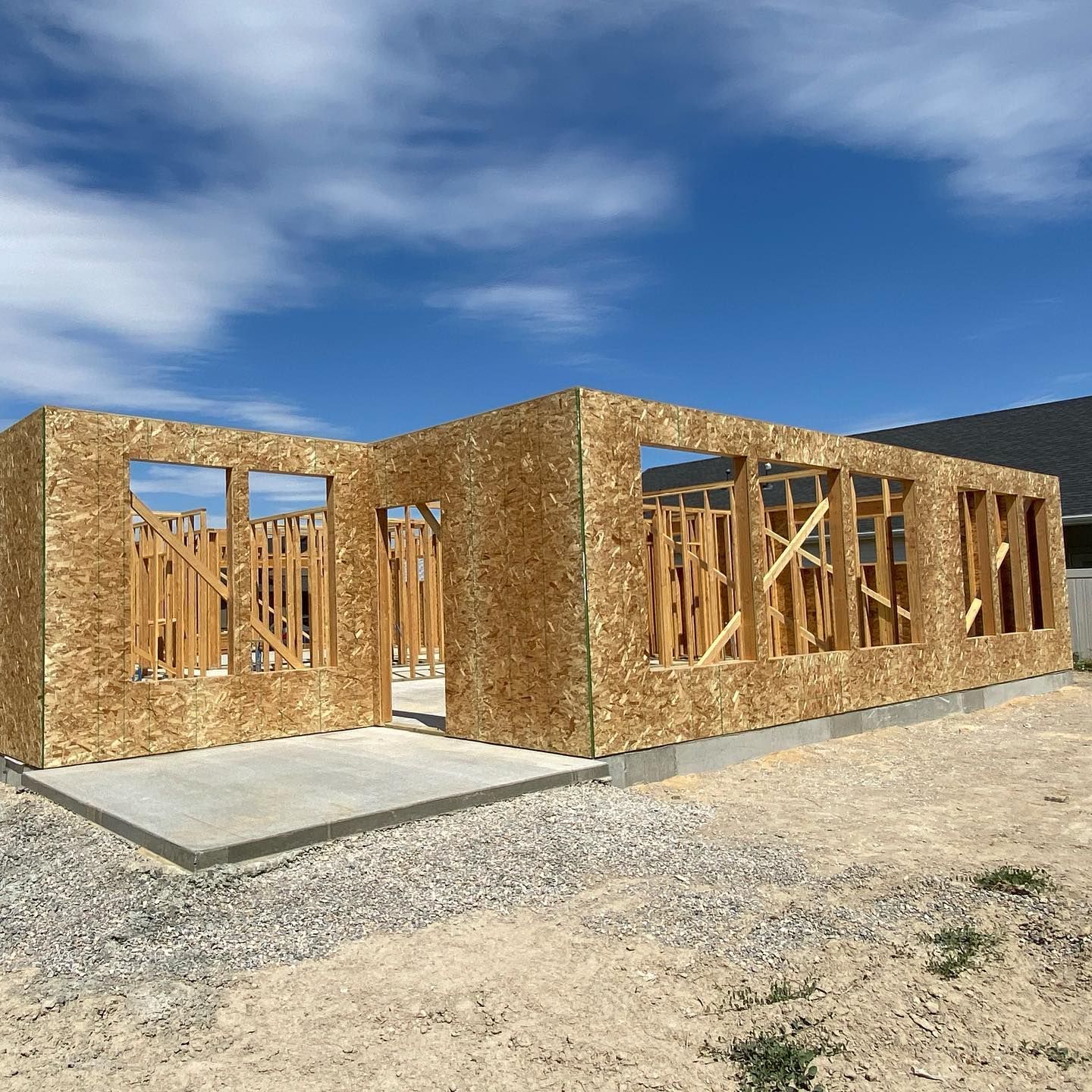 Wood frame house under construction on a concrete foundation, with blue sky.